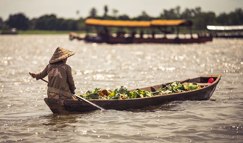 A-woman-rowing-a-wooden-boat-full-of-vegetables on the Mekong River